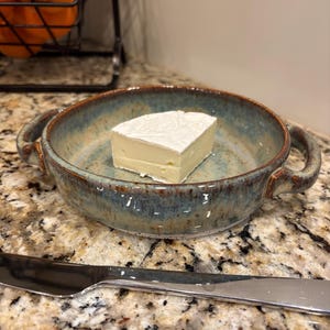 May include: A white ceramic mug with a black handle and the text "But First, Coffee" in a black, handwritten-style font. The mug is on a white surface.