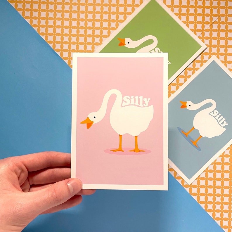 K&ouml;nnte beinhalten: Drei Karten in rosa, gr&uuml;n und blau mit einer wei&szlig;en G&auml;nseillustration und dem Wort "Silly" auf jeder Karte.
