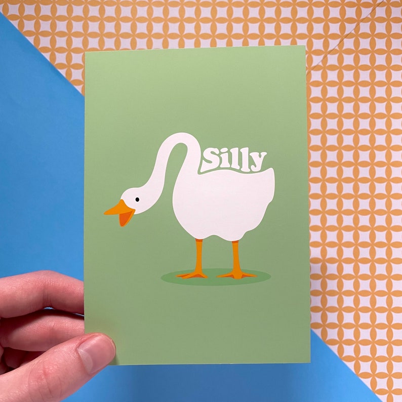 K&ouml;nnte beinhalten: Eine gr&uuml;ne Karte mit einer Illustration einer wei&szlig;en Gans. Die Gans hat den Kopf zur&uuml;ckgedreht und das Wort "Silly" steht auf ihrem R&uuml;cken.