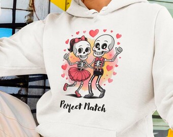 May include: White hoodie featuring a cartoon illustration of two dancing skeletons. The skeletons are holding hands, surrounded by hearts, and wearing a bow tie and a tutu. The text "Perfect Match" is printed below the illustration.