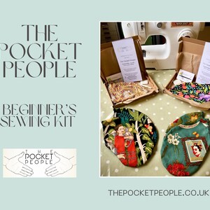 Op de afbeelding: Een beginnersnaaiset van The Pocket People, met twee stoffen mondmaskers met kleurrijke bloemen- en Frida Kahlo-ontwerpen. De set wordt geleverd in een bruine kartonnen doos met instructies en materialen. Het logo van The Pocket People is zichtbaar op de doos en in de afbeelding.