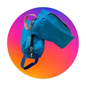 Può includere: Una borsa blu brillante con un cinturino blu abbinato e un manico rosa. La borsa ha una cerniera nera e un tirazip argentato. Lo sfondo è un gradiente di rosa, arancione e viola.