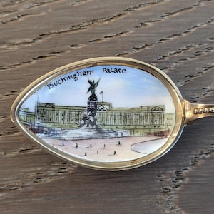 May include: A silver spoon with a painted image of Buckingham Palace on the front. The spoon has a beaded handle.