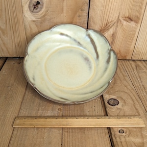 Puede incluir: Un tazón de cerámica amarillo claro con un borde festoneado y un diseño de remolino. El tazón está sobre una superficie de madera.