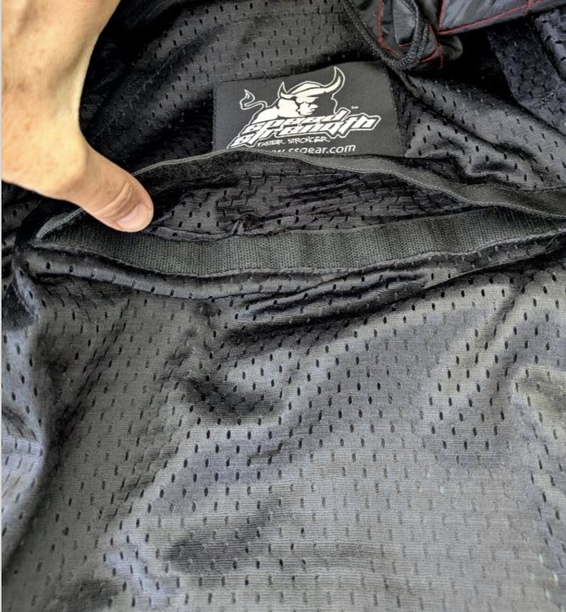 May include: Black mesh fabric with a Speed and Strength logo patch. The patch features a bull graphic and the text "Speed and Strength". The interior of the garment is visible, showing a pocket.