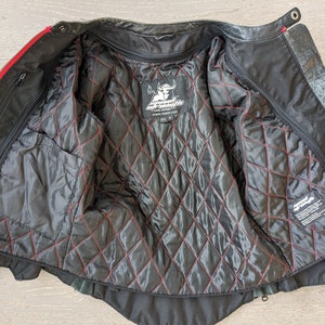 May include: Black leather motorcycle jacket with red accents. The interior features a quilted black lining with red stitching. The jacket has multiple pockets and a zipper closure. The brand logo is visible on the inside.