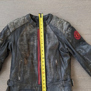 May include: A distressed black leather motorcycle jacket with a red zipper and the text "SPEED AND STRENGTH". The jacket has a round collar, zippered pockets, and a patch on the sleeve. The jacket measures approximately 24 inches in length.