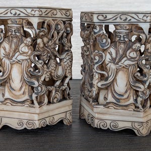 Peut inclure: Deux porte-stylos sculptés en blanc cassé. Chacun présente un relief détaillé d'une figure barbue tenant un enfant, avec des dragons et d'autres personnages. La conception ajourée permet à la lumière de passer à travers.