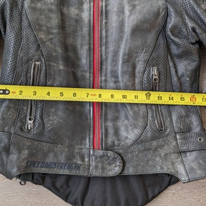 May include: A distressed black leather motorcycle jacket with a red zipper and the text "SPEED AND STRENGTH". The jacket has multiple zippered pockets and perforated panels. The jacket measures approximately 16 inches across.
