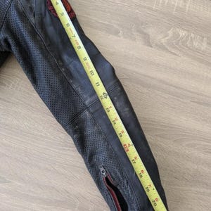 May include: Black leather motorcycle jacket sleeve with a red and black patch. The sleeve is approximately 23 inches long, featuring a zipper and perforated detailing. The jacket is worn and distressed.