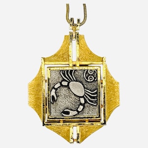 May include: Gold-toned pendant necklace featuring a square frame with a textured finish. The pendant showcases a silver-toned square with a crab zodiac symbol. The necklace has a delicate gold chain.