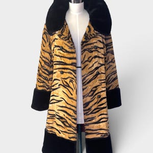 May include: A long coat featuring a gold and black tiger stripe pattern. The garment includes a large black faux fur collar, black faux fur cuffs at the sleeves, and a wide black faux fur hem. It has a double-breasted front with black buttons.