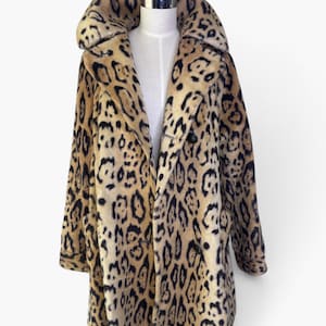 May include: A long-sleeved coat featuring a tan and black leopard print pattern. The coat has a large, wide collar, a double-breasted front closure with dark buttons, and two side pockets. The garment is displayed on a white mannequin torso.