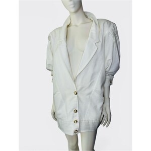 May include: A white blazer with gold buttons. The jacket features a classic lapel collar, three-quarter sleeves, and a tailored fit. The garment is displayed on a mannequin against a white background. The blazer has a button closure and two front pockets.