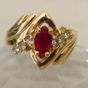 May include: A gold ring with a large red marquise-shaped gemstone surrounded by smaller clear gemstones.