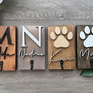 May include: Four wooden signs with hooks, each featuring a different dog's name and paw print. The names are Mila, Nadine, Kai, and Mika.