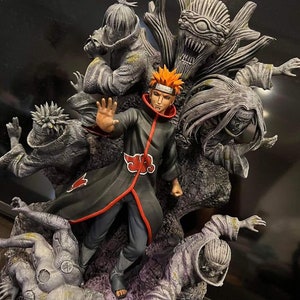 May include: A detailed figurine of a character from the anime Naruto, with orange hair and a red cloud on his chest, surrounded by other characters in a dark, rocky setting.