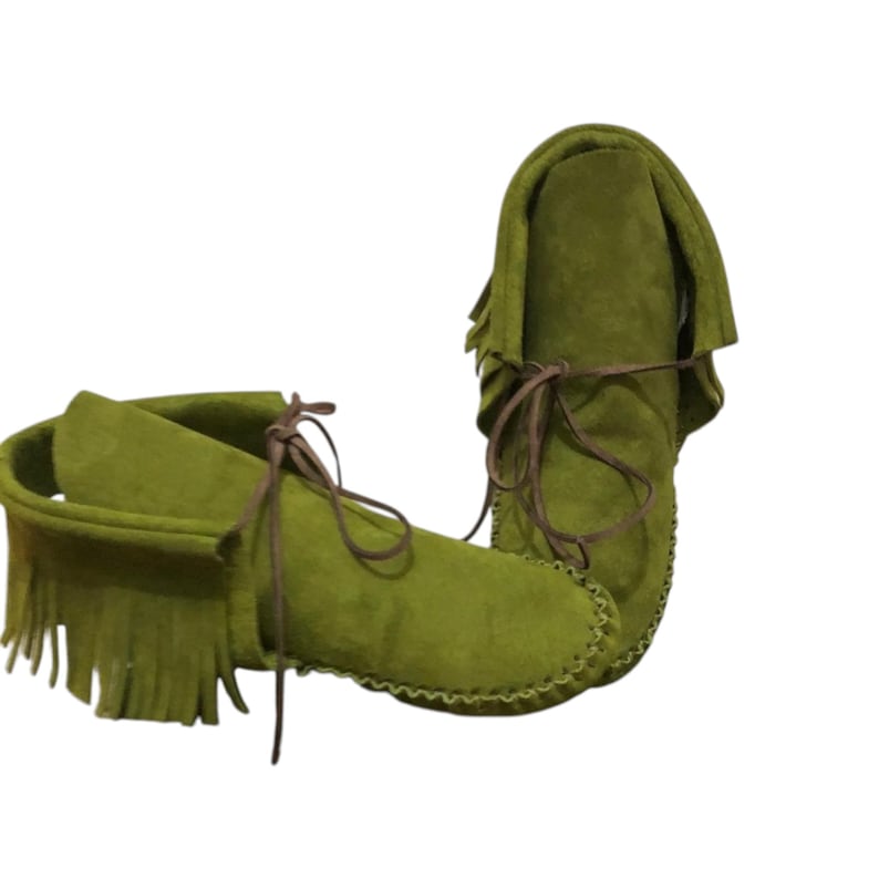 May include: Olive green suede moccasin boots with brown leather laces. The boots feature a fringe detail around the ankle and a stitched sole. The boots are made of soft suede material.