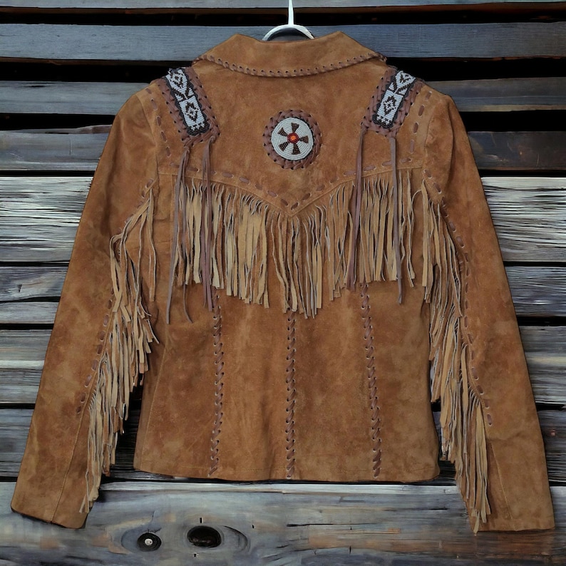 Back view of women’s vintage suede fringe jacket featuring handmade beaded details, genuine suede leather, and soft inside lining. This boho Western jacket showcases long fringe across the back and sleeves with Southwestern-inspired design and rustic cowgirl fashion appeal. Perfect tan suede jacket for rodeo events, country concerts, festival outfits, Western wear lovers, and bohemian fashion styling. Authentic handmade fringe suede coat with timeless vintage Western charm.