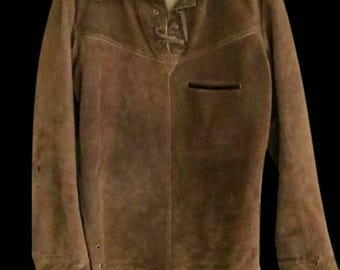 May include: A brown suede shirt with a collared neckline and long sleeves. The shirt features a lace-up closure at the chest and a small pocket. The garment is hanging on a clear plastic hanger.