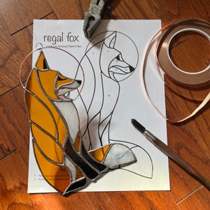 May include: A stained glass fox pattern with numbered pieces, copper foil tape, a glass cutter, and a copper wire for hanging. The pattern is titled "regal fox" and is a pattern by SunKissed Stained Glass.
