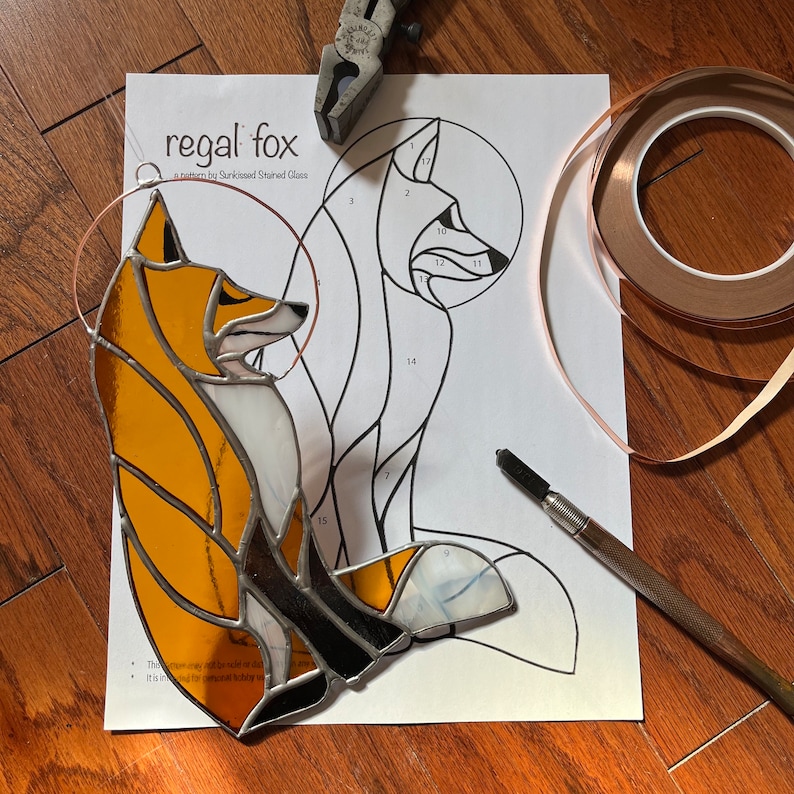 May include: A stained glass fox pattern with numbered pieces, copper foil tape, a glass cutter, and a copper wire for hanging. The pattern is titled "regal fox" and is a pattern by SunKissed Stained Glass.