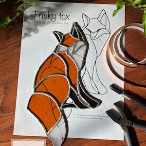 May include: A stained glass pattern for a fox, with the finished piece in the foreground. The pattern is labeled "Frisky fox" and includes the text "This pattern may not be sold or distributed in any way. It is intended for personal hobby use only."