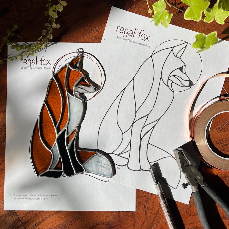 May include: A stained glass pattern for a regal fox, with a black and white outline of the fox on a white sheet of paper. The pattern is titled "regal fox" and includes the text "a pattern by Sunkissed Stained Glass".