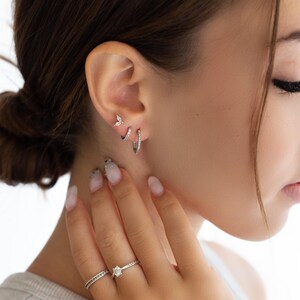 Pode incluir: Uma mulher usando um anel de prata com um pequeno diamante e dois brincos de prata com pequenos diamantes. Os brincos s&atilde;o um pequeno design de borboleta e um aro.