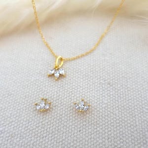 Op de afbeelding: Een gouden ketting met een klein hangertje met een cluster van heldere zirkonia-stenen. Passende oorbellen met een vergelijkbaar ontwerp zijn ook inbegrepen.