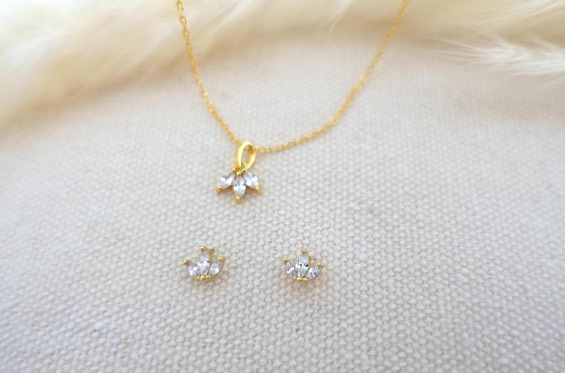 Op de afbeelding: Een gouden ketting met een klein hangertje met een cluster van heldere zirkonia-stenen. Passende oorbellen met een vergelijkbaar ontwerp zijn ook inbegrepen.