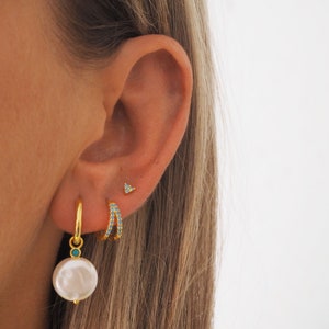 May include: Gold hoop earrings with turquoise stones, a gold hoop earring with a pearl charm, and a small gold triangle stud earring.