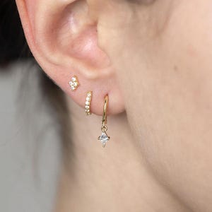 May include: Gold earrings with small diamond-shaped stones. The earrings are a hoop style with a dangling diamond-shaped stone.