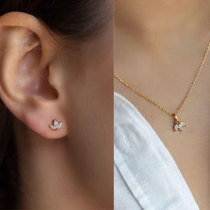 Op de afbeelding: Een paar gouden oorbellen en een gouden ketting met een klein, delicaat hangertje met een cluster van heldere edelstenen. Het hangertje heeft de vorm van een bloem.