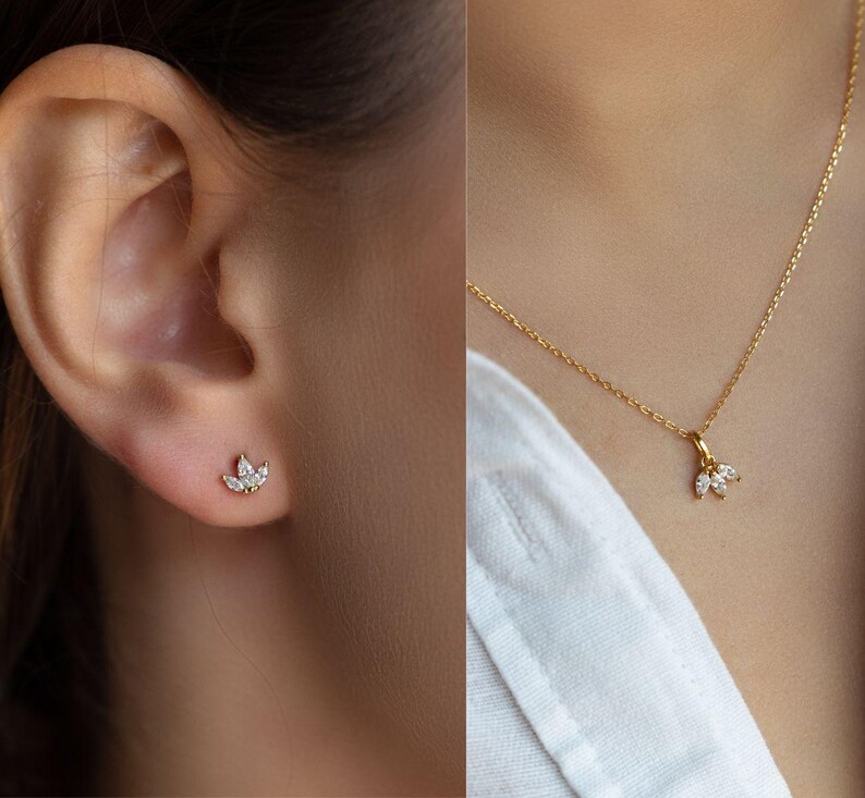 Op de afbeelding: Een paar gouden oorbellen en een gouden ketting met een klein, delicaat hangertje met een cluster van heldere edelstenen. Het hangertje heeft de vorm van een bloem.