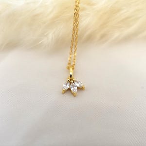 Op de afbeelding: Een gouden ketting met een klein hangertje met drie heldere, peervormige stenen.
