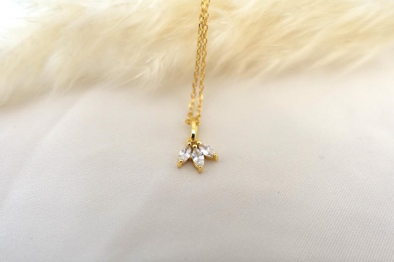 Op de afbeelding: Een gouden ketting met een klein hangertje met drie heldere, peervormige stenen.