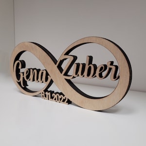 May include: A wooden infinity symbol with the names "Gena" and "Zuber" carved into it. The date "8.11.2022" is also carved into the symbol.