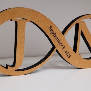 May include: A wooden infinity symbol with the letters "J" and "N" cut out. The date "September 9, 2023" is engraved on the symbol.