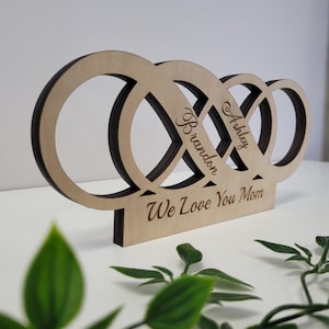 May include: Wooden cutout of three interlocking rings with the names Ashley and Brandon inscribed on them. The bottom of the cutout reads "We Love You Mom".