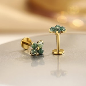 May include: Two gold-colored, gemstone earrings. One earring features a cluster of four green gemstones, while the other has a single post with a cluster of five green gemstones. The earrings are set against a neutral background.