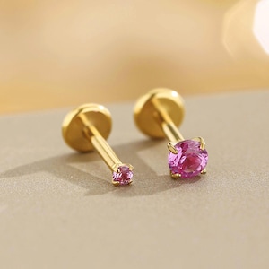 K&ouml;nnte beinhalten: Zwei goldfarbene Ohrstecker mit rosa Edelsteinen. Ein Ohrring hat einen kleinen rosa Edelstein, der andere einen gr&ouml;&szlig;eren, runden rosa Edelstein. Die Ohrringe sind vor einem neutralen Hintergrund platziert.