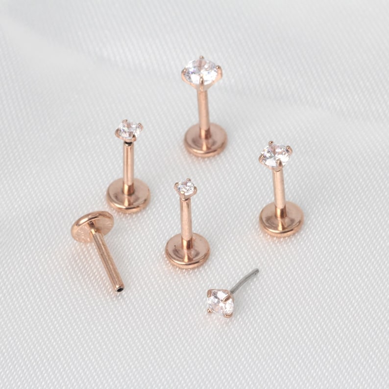 Op de afbeelding: Zes lichaamssieraden van ros&eacute;goud met heldere zirkonia-stenen. De stukken zijn in verschillende maten en stijlen verkrijgbaar, waaronder een oorbel, een labret en een helixring.