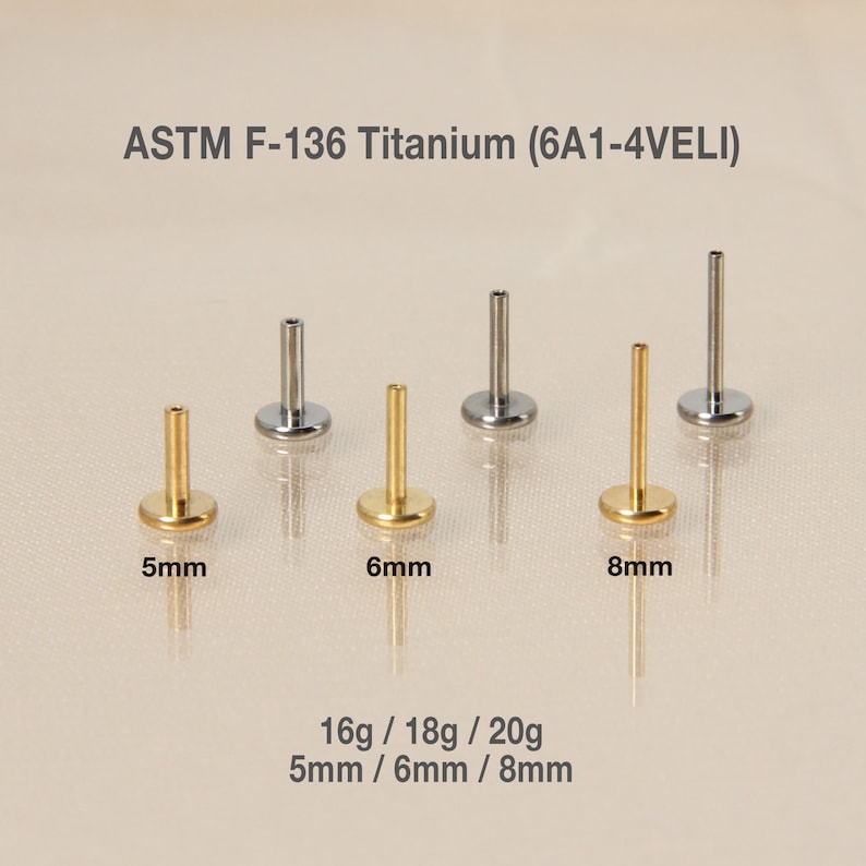 May include: Six titanium body jewelry pieces in gold and silver, with a flat base and a straight post. The pieces are arranged in three sizes: 5mm, 6mm, and 8mm. The text "ASTM F-136 Titanium (6A1-4VELI)" is at the top of the image. The text "16g/18g/20g 5mm/6mm/8mm" is at the bottom of the image.
