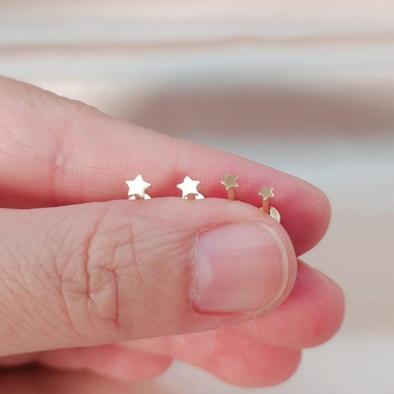 Op de afbeelding: Vier gouden stervormige oorbel studs, gerangschikt in een rij, op een vinger.