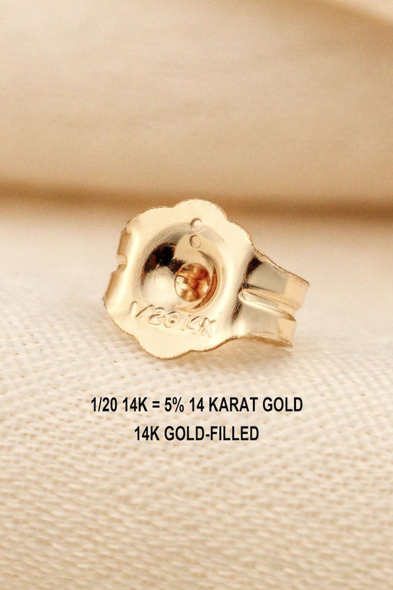 Puede incluir: Un cierre de pendiente de color dorado con borde festoneado, que presenta el texto grabado 1/20 14K. Debajo del cierre, el texto indica 1/20 14K = 5% 14 KARAT GOLD y 14K GOLD-FILLED, se&ntilde;alando la composici&oacute;n del componente met&aacute;lico.