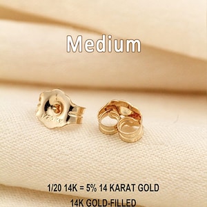 Puede incluir: Dos cierres de pendiente de color dorado con un dise&ntilde;o de borde festoneado. El texto "Medium" aparece sobre los art&iacute;culos, y el texto "1/20 14K = 5% 14 KARAT GOLD" y "14K GOLD-FILLED" est&aacute; impreso debajo de los cierres sobre la superficie texturizada.