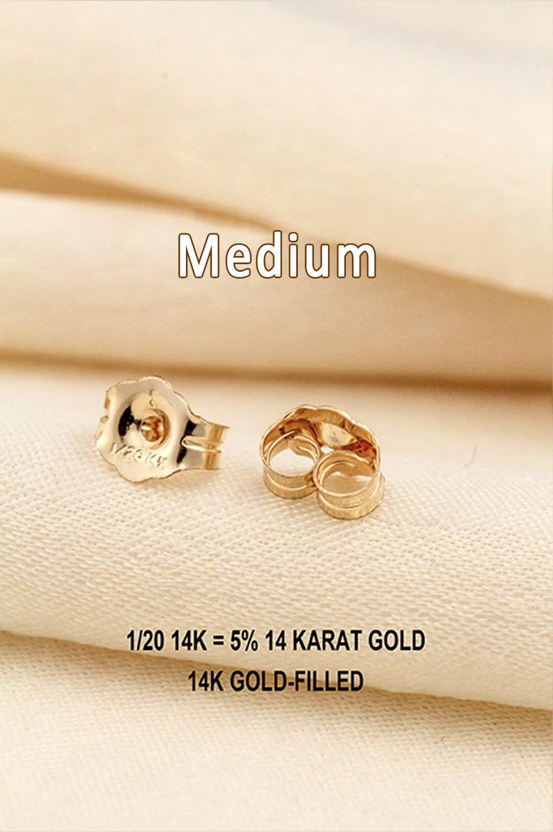 Puede incluir: Dos cierres de pendiente de color dorado con un dise&ntilde;o de borde festoneado. El texto "Medium" aparece sobre los art&iacute;culos, y el texto "1/20 14K = 5% 14 KARAT GOLD" y "14K GOLD-FILLED" est&aacute; impreso debajo de los cierres sobre la superficie texturizada.