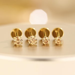 Peut inclure: Quatre boucles d'oreilles à clous dorées avec des pierres précieuses couleur champagne. Les boucles d'oreilles sont disposées en rangée, mettant en valeur les différentes tailles des pierres. Les clous ont un design simple et élégant, idéal pour un usage quotidien ou des occasions spéciales.