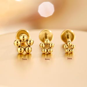 May include: Three gold-tone stud earrings, each featuring a flower-shaped design made of five small spheres. The earrings are labeled with sizes 5mm, 4mm, and 3mm, indicating the diameter of the flower-shaped head of each individual stud earring.